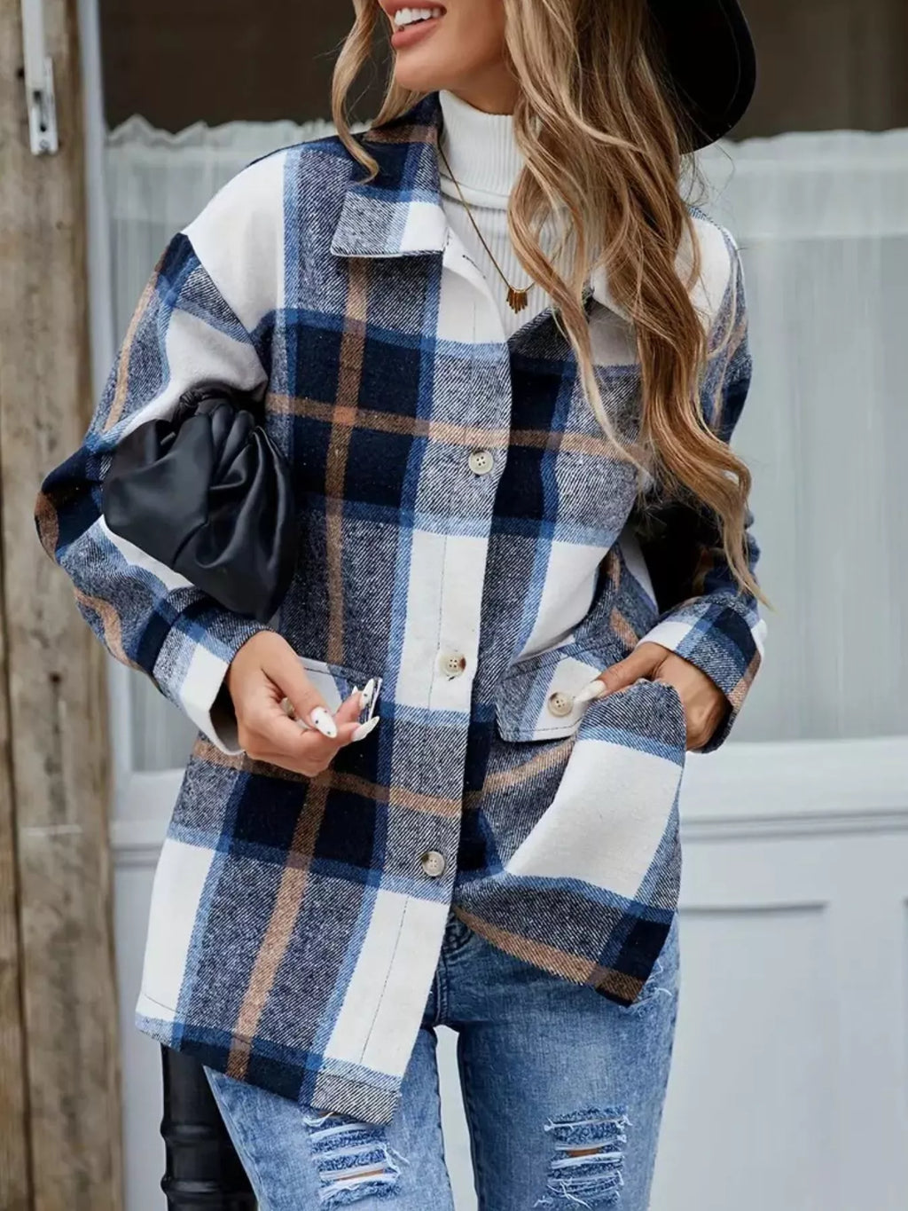 Front view of the blue plaid shacket, with one hand in a pocket and a black clutch under an arm.
