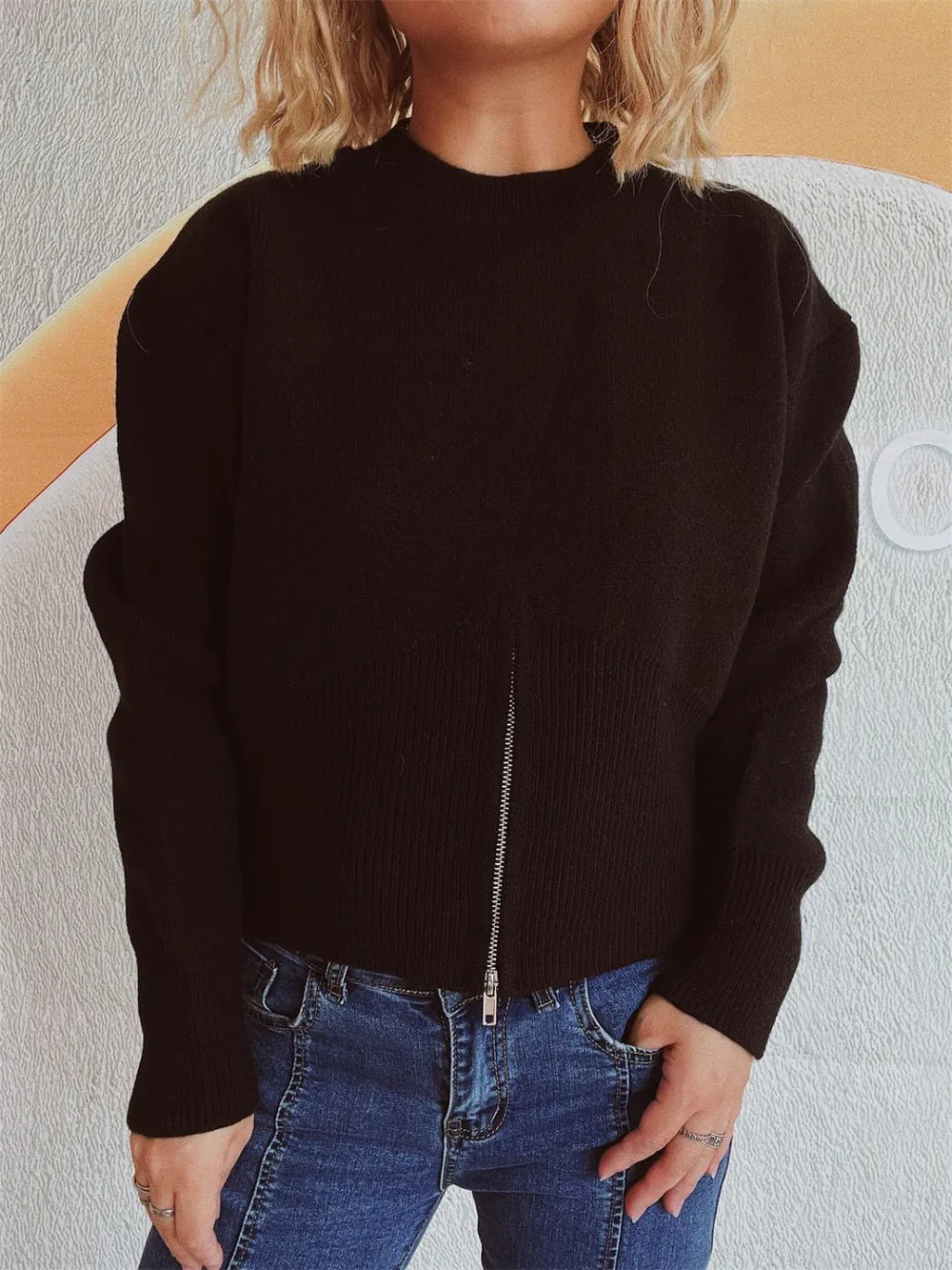 Black half-zip knit sweater with the zip partly open, worn with hands on hips.