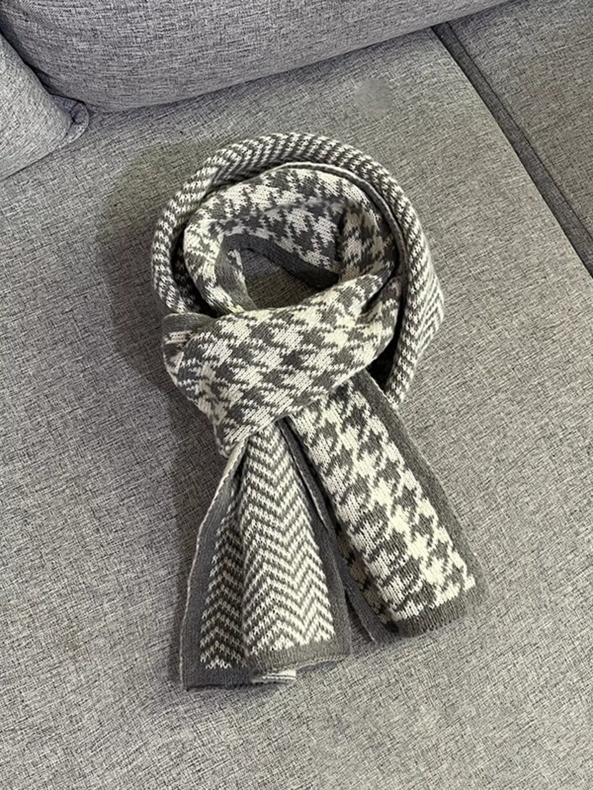 Grey houndstooth and chevron scarf looped loosely, laid on a grey couch.
