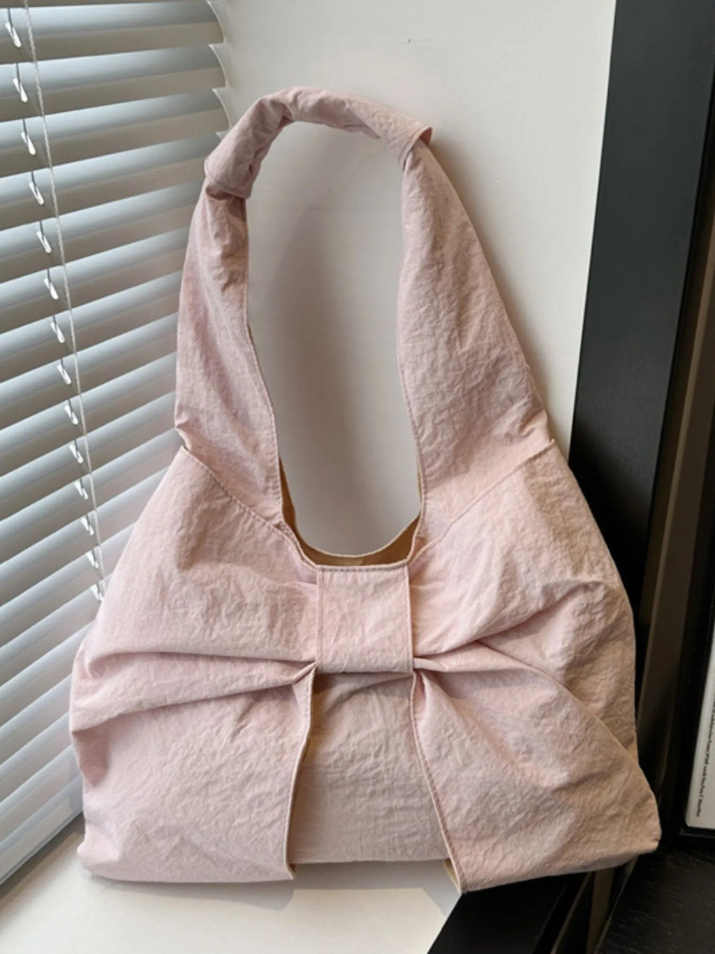 Pale pink bow shoulder bag standing near a window.