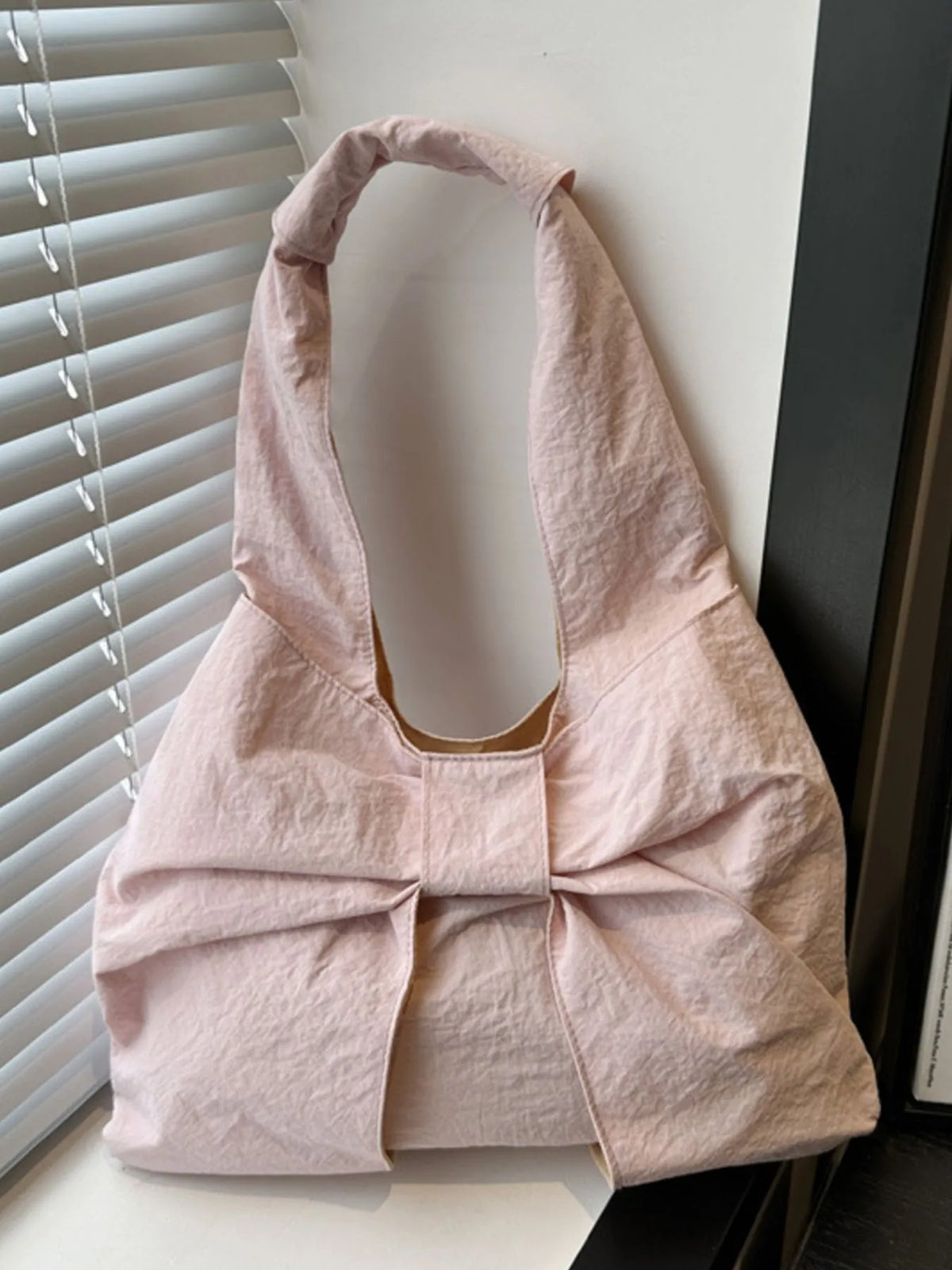 Pale pink bow shoulder bag standing near a window.