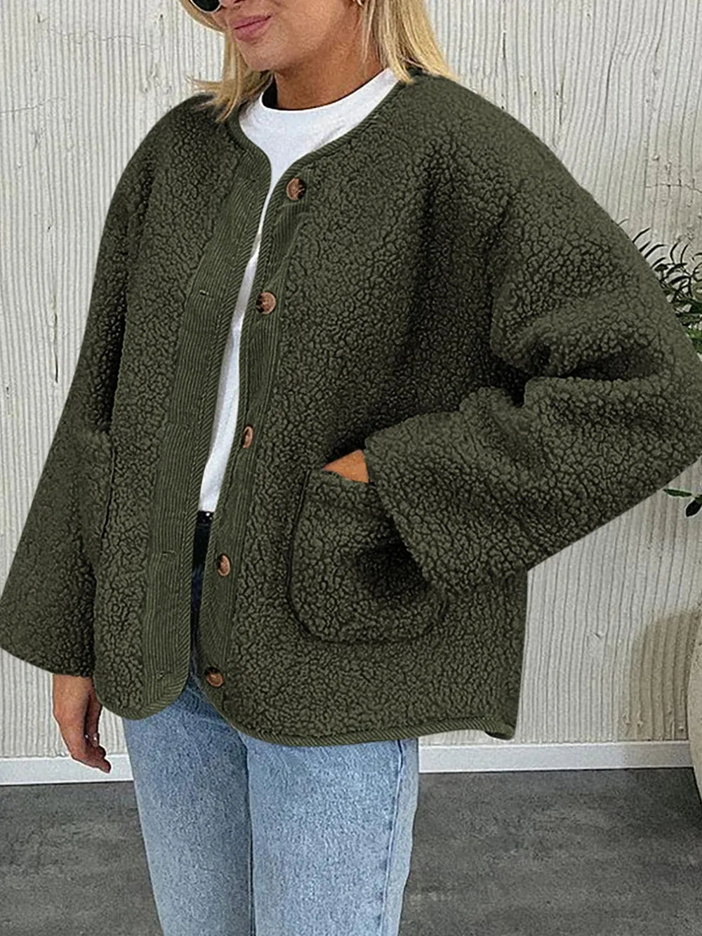 Olive green textured jacket worn with a white T-shirt and jeans, with one hand in a pocket.