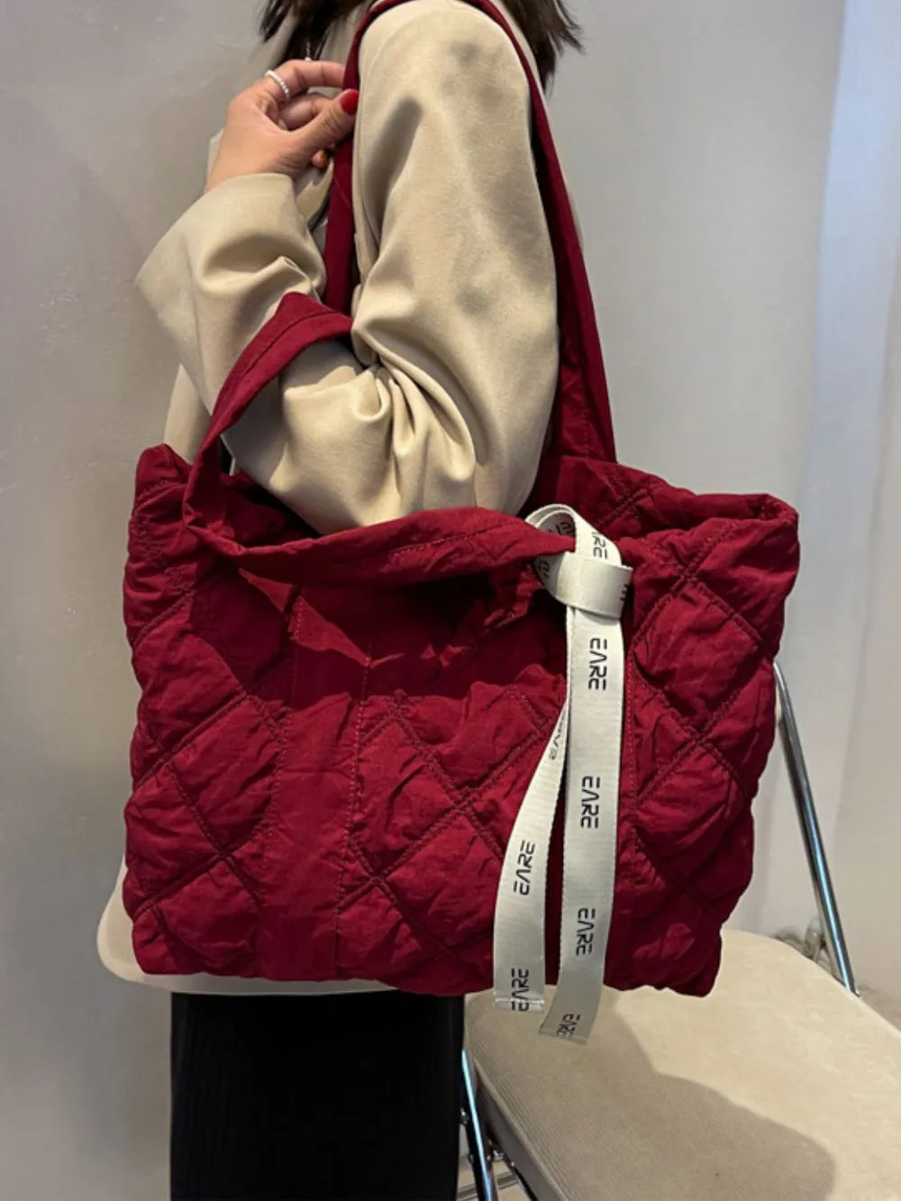 Burgundy quilted tote worn on the shoulder with a beige jacket.