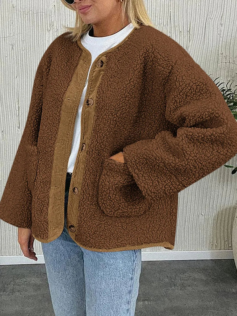 Brown textured jacket worn with a white T-shirt and jeans, with one hand in a pocket.