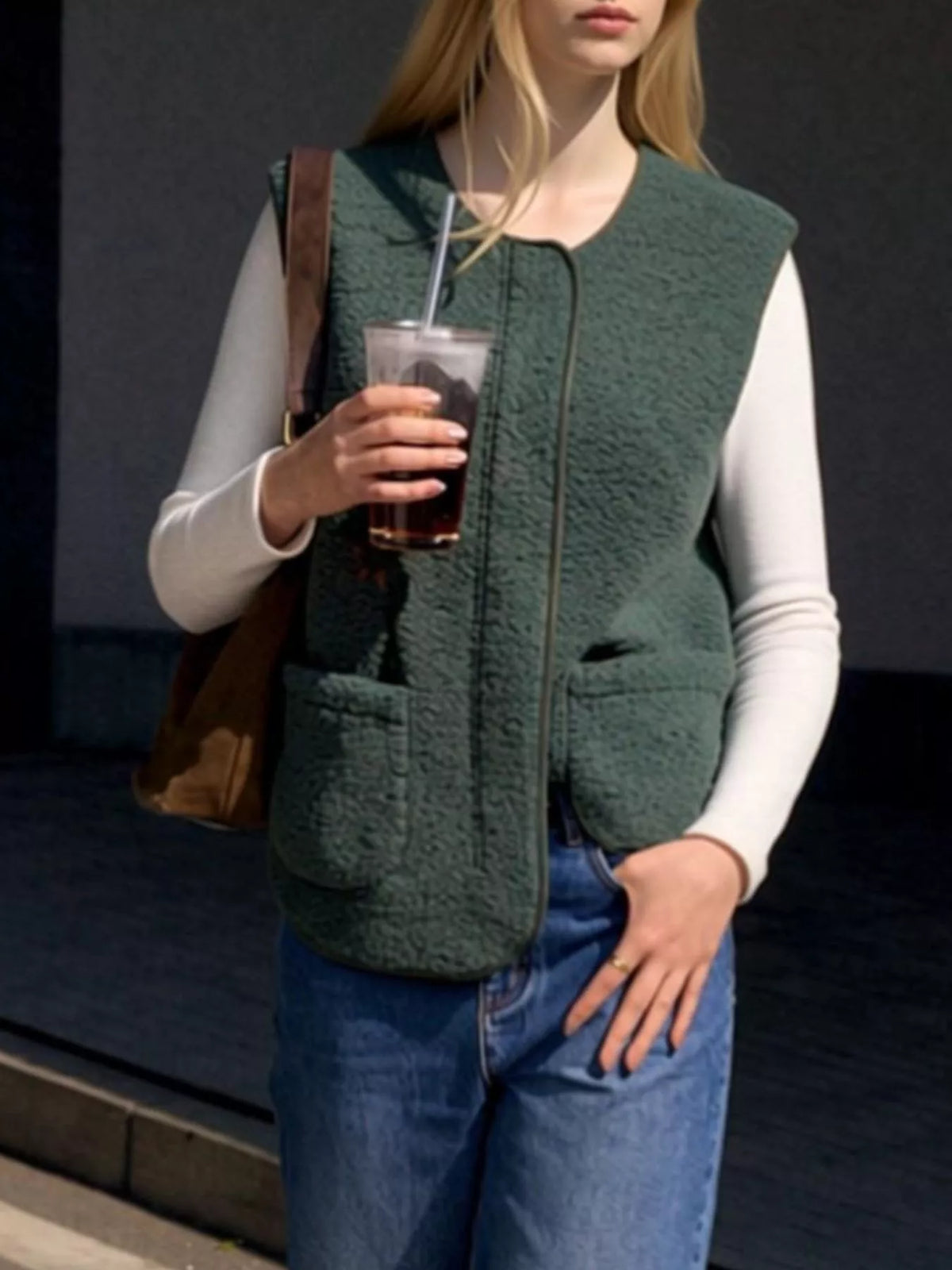 Dark Green sherpa vest worn over a white top with jeans, holding an iced coffee.