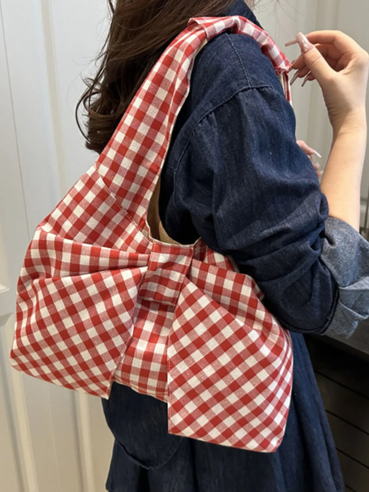 Side view of the red and white checked bow shoulder bag worn with a dark blue outfit.