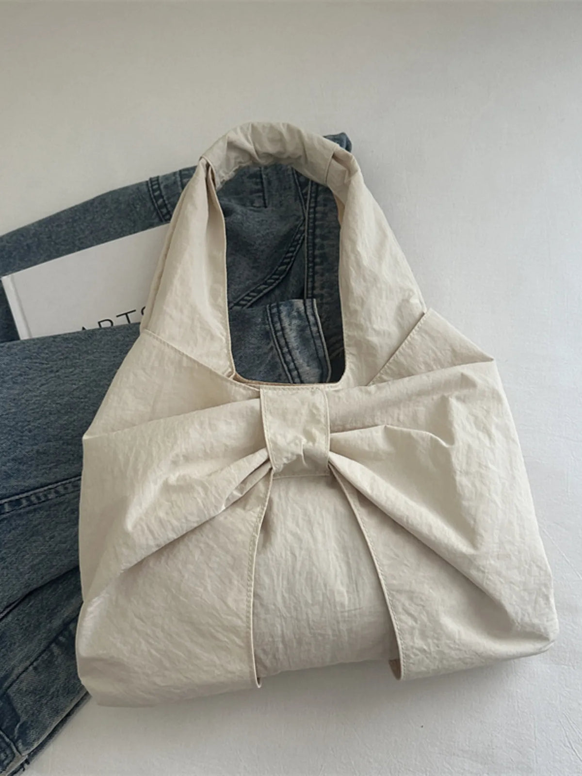 Cream bow shoulder bag resting against denim on a chair.
